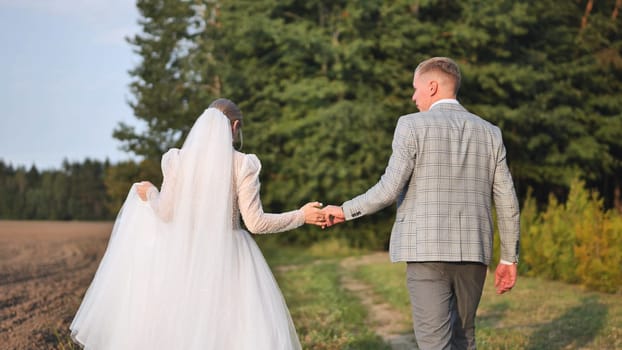 Newlywed couple holding hands walking down a path on their wedding day, celebrating their new life together