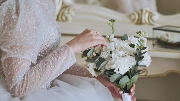 Elegant bride wearing white wedding gown, holding eucalyptus bouquet, sporting delicate golden wedding band