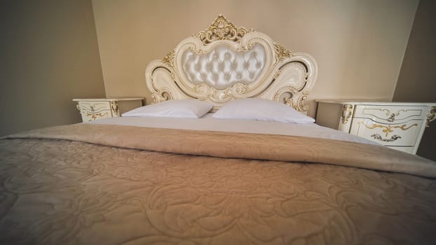 Luxurious beige king size bed with ornate headboard, bedside tables, and soft blanket, creating romantic atmosphere for wedding night or honeymoon