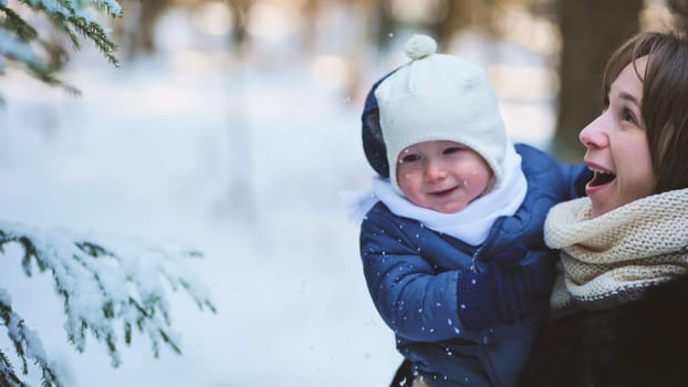 Happy mother holding her smiling baby, enjoying a winter day as snowflakes gently fall, creating a picturesque scene of joy and togetherness
