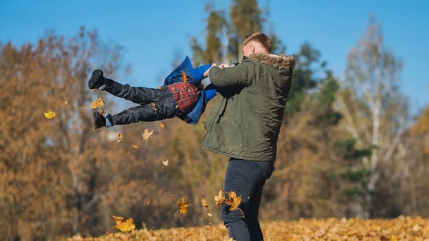 Father and son enjoying playful moments together in a vibrant park, surrounded by colorful autumn foliage on a sunny day