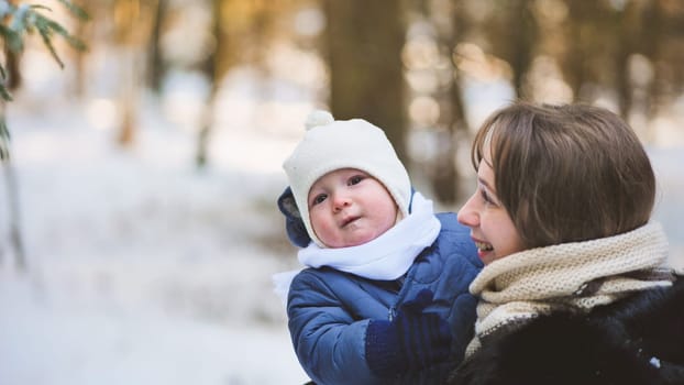 Mother cuddling newborn, walking through snow covered forest, sharing tender moment amid pristine winter landscape, radiating maternal warmth