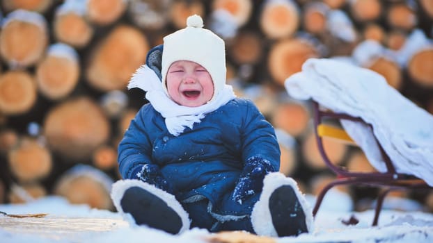 Tearful infant wailing, bundled in snowsuit beside wooden sled, snowy landscape with stacked firewood surrounding sad child