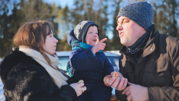 Happy family enjoying a bright winter day outdoors, laughing and sharing tangerines amidst the snowy landscape, creating joyful memories