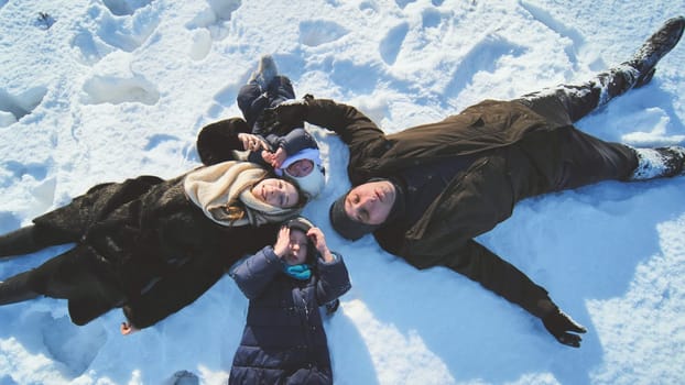 Winter family bonding, parents with children creating snow angels, laughing and playing outdoors during snowy day