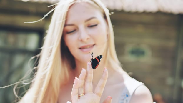 Blonde woman enjoying a sunny summer day, gently holding a red admiral butterfly on her finger, embodying beauty and tranquility in nature