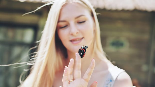 Blonde woman delicately balancing vibrant butterfly on fingertip, experiencing serene moment amid lush outdoor summer landscape