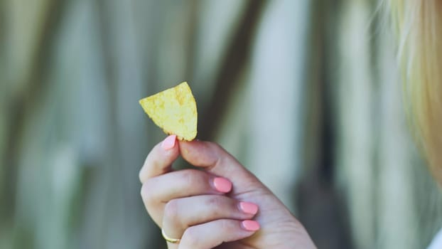 Woman with perfectly manicured nails holding a single golden potato chip, preparing for a deliciously crispy snack moment