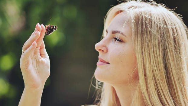 Young blonde woman holding a butterfly delicately on her finger, savoring the beauty of nature on a sunny summer day