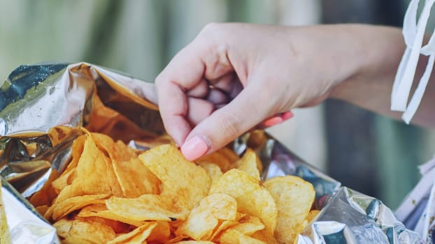 Woman reaching into a foil bag, savoring a crispy potato chip and indulging in a delicious salty snack filled with flavor