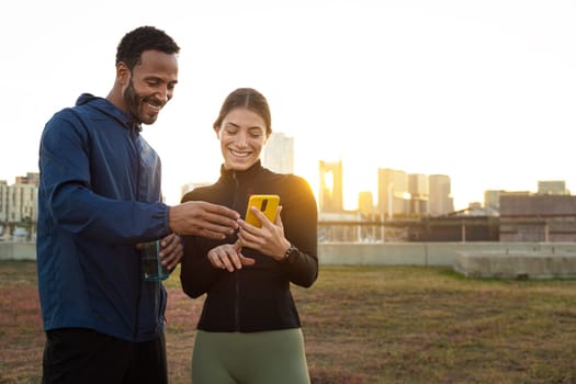 Two athletes checking their fitness app on a smartphone after training outdoors