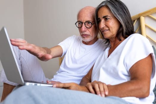 Mature heterosexual couple using laptop together in bed. Looking for information online. Lifestyle and technology concepts.