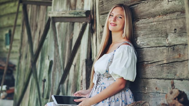 Young woman using a digital tablet while leaning against a rustic wooden wall, showcasing a blend of tradition and technology