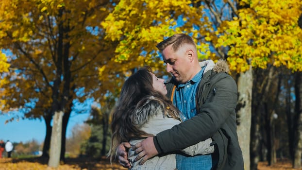 Romantic couple embracing in a vibrant autumn park, surrounded by golden foliage, enjoying a tender moment together