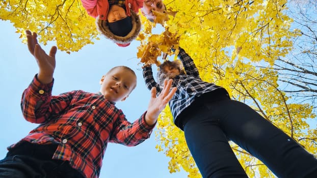 Happy family holding yellow maple leaves, playing together in autumn park, low angle view