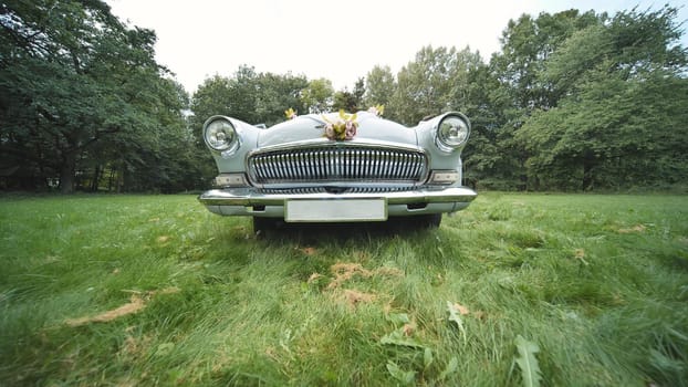 Light blue vintage car decorated with flower bouquets, parked on a green lawn in a park, ready for a wedding ceremony
