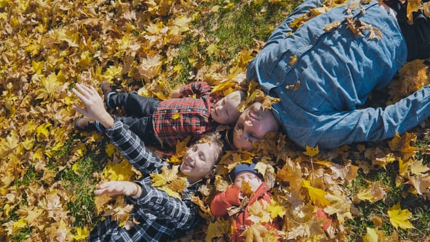 Happy family enjoying a sunny autumn day lying down and playing in a park full of colorful leaves