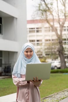 A joyful Muslim businesswoman in a hijab, excitedly holding her laptop in an outdoor setting, reflecting her passion for work.