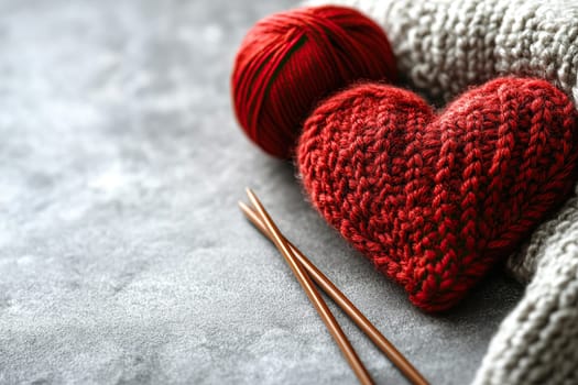 A knitted red heart with knitting needles and a ball of red thread lies on a concrete surface. Valentine's Day. A DIY gift.