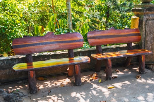 Front view of a park bench made of dark brown wood on the stone pavement of the park complex