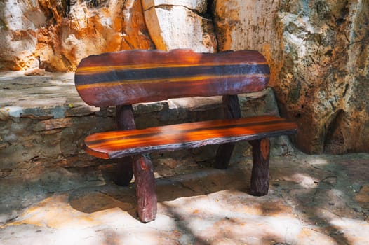 Front view of a park bench made of dark brown wood on the stone pavement of the park complex