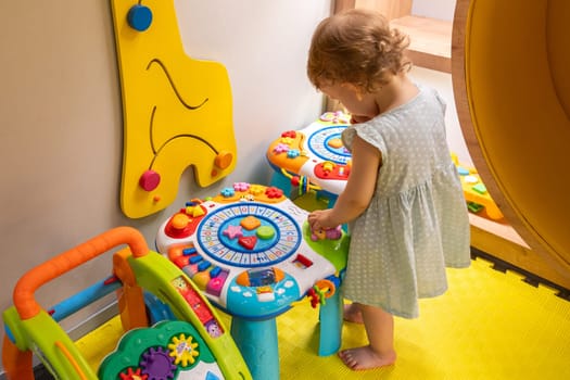 Toddler exploring a colorful educational activity table in a bright playroom, discovering shapes and sounds. Concept of interactive learning and encouraging creativity in early development