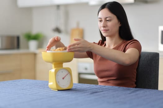 Asian woman weighing food using scale on a table in the kitchen at home