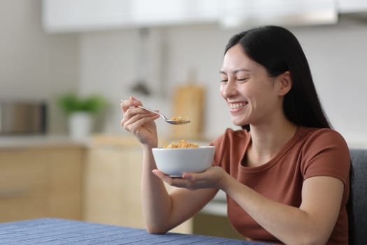 Happy asian woman eating cereals in a kitchen in the kitchen at home