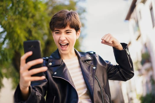 A young person in a stylish leather jacket happily takes a selfie outdoors, enjoying a vibrant atmosphere filled with energy and creating a cherished moment to remember and treasure