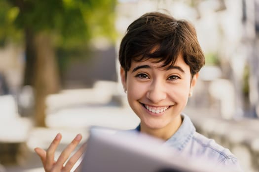 A joyful young woman is smiling brightly while engaged with her tablet outdoors, demonstrating the happiness, connectivity, and vibrant engagement that characterize our modern life in a digital world