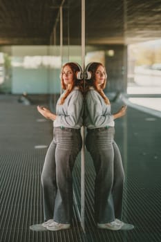 In a vibrant urban setting, a stylish woman poses by a reflective surface, wearing trendy headphones and casual attire, blending fashion with culture as she enjoys her favorite music
