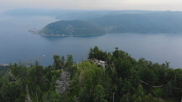 Wooden observation deck perched amid forest foliage, revealing panoramic lakeside scenery of lake baikal and listvyanka port from aerial perspective