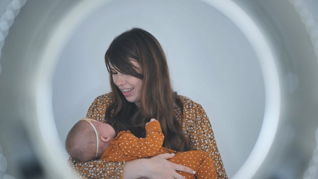 Soft lit studio portrait showing maternal warmth, female parent gently holding sleeping infant with professional lighting technique