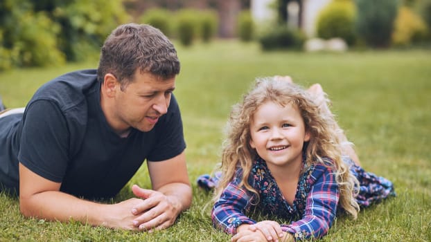 Father and daughter lying on grass, enjoying a playful moment together during family day in their garden
