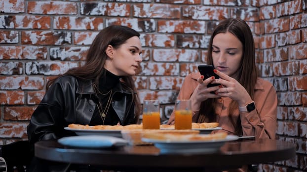 A girl peeks into her friend's smartphone at a coffee shop