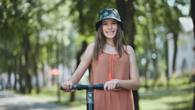 Teenage girl smiling, riding electric scooter through sunny park, green landscape reflecting summer leisure and youthful energy