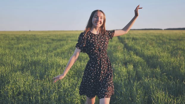 Happy young woman in a floral dress dancing in a green field, enjoying the sunset and the beauty of nature