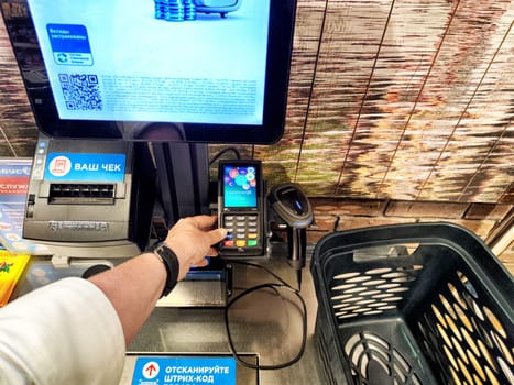 Kirov, Russia - August 28, 2024: Shopper using a self-service checkout terminal to complete a purchase at a grocery store in Kirov, Russia's vibrant market.