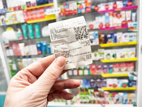Kirov, Russia - December 11, 2024: A hand holds a receipt from a pharmacy while shelves filled with health products and medications are visible in the background.