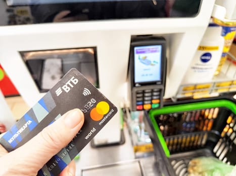 Kirov, Russia - December 18, 2024: Customer uses a contactless card to pay at a self-service checkout station in a grocery store, surrounded by shopping items.