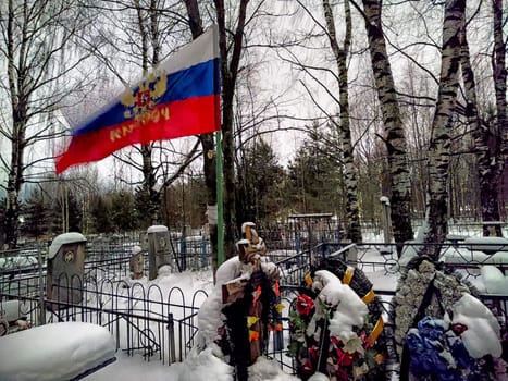 Kirov, Russia - December 29, 2024: Snow blankets a cemetery where a Russian flag marks a grave, surrounded by wreaths in remembrance of fallen soldiers during conflict or Russia and Ukraine