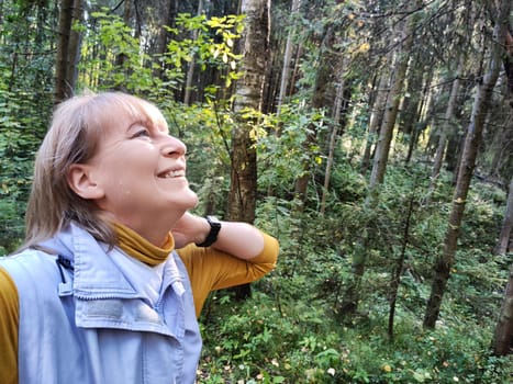 A middle aged woman smiles while exploring a serene forest, appreciating the beauty of nature on her excursion.