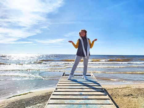 Woman in casual attire stands on a wooden pier, contemplating life while enjoying the serene ocean views during autumn's beauty.