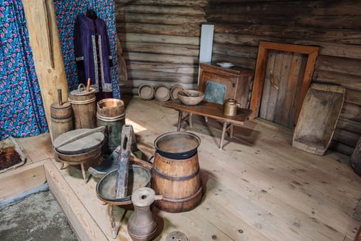 Weathered wooden barrels, handcrafted bowls, vintage tools adorning traditional russian izba interior with folk clothing draped nearby