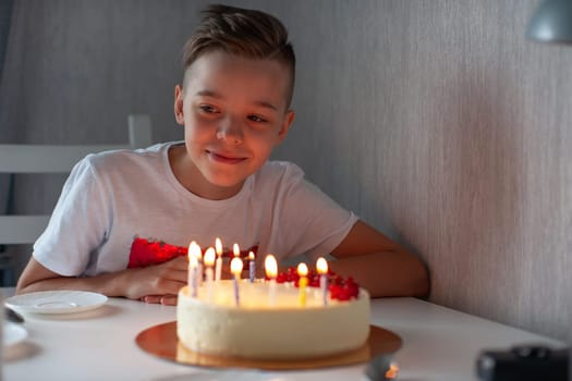 Smiling young boy leaning on a table with a lit birthday cake, enjoying a joyful celebration in a cozy setting.