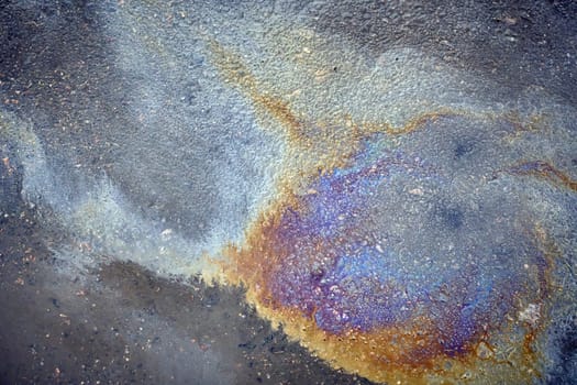 Gasoline or oil spill creating colorful patterns on asphalt road.