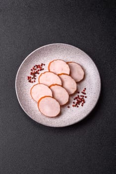 Delicious fresh ham cut into round slices with salt, spices and herbs on a dark concrete background