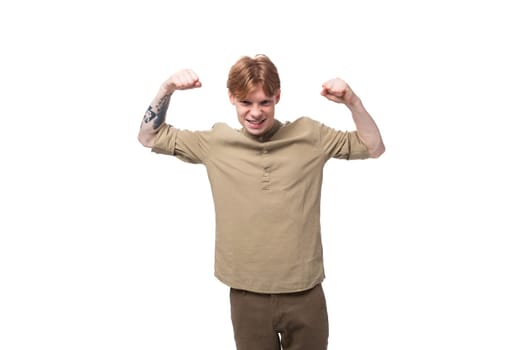 a young slender red-haired caucasian guy dressed in a khaki short-sleeve shirt shows muscles.