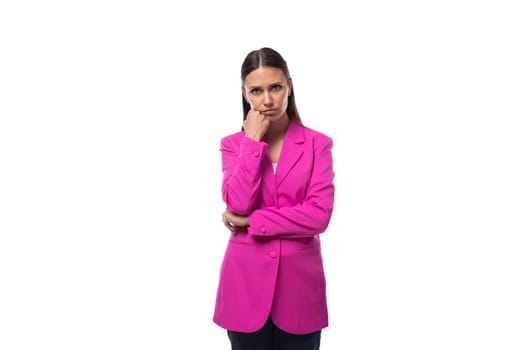 young smart office worker woman with black hair dressed in a pink jacket stands thoughtfully.