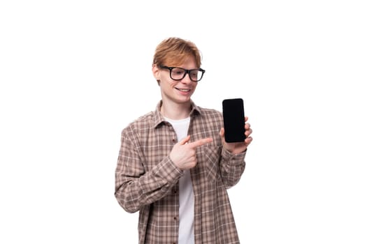 young successful european student man with red short hair and glasses shows the screen of a mobile phone with a mockup.